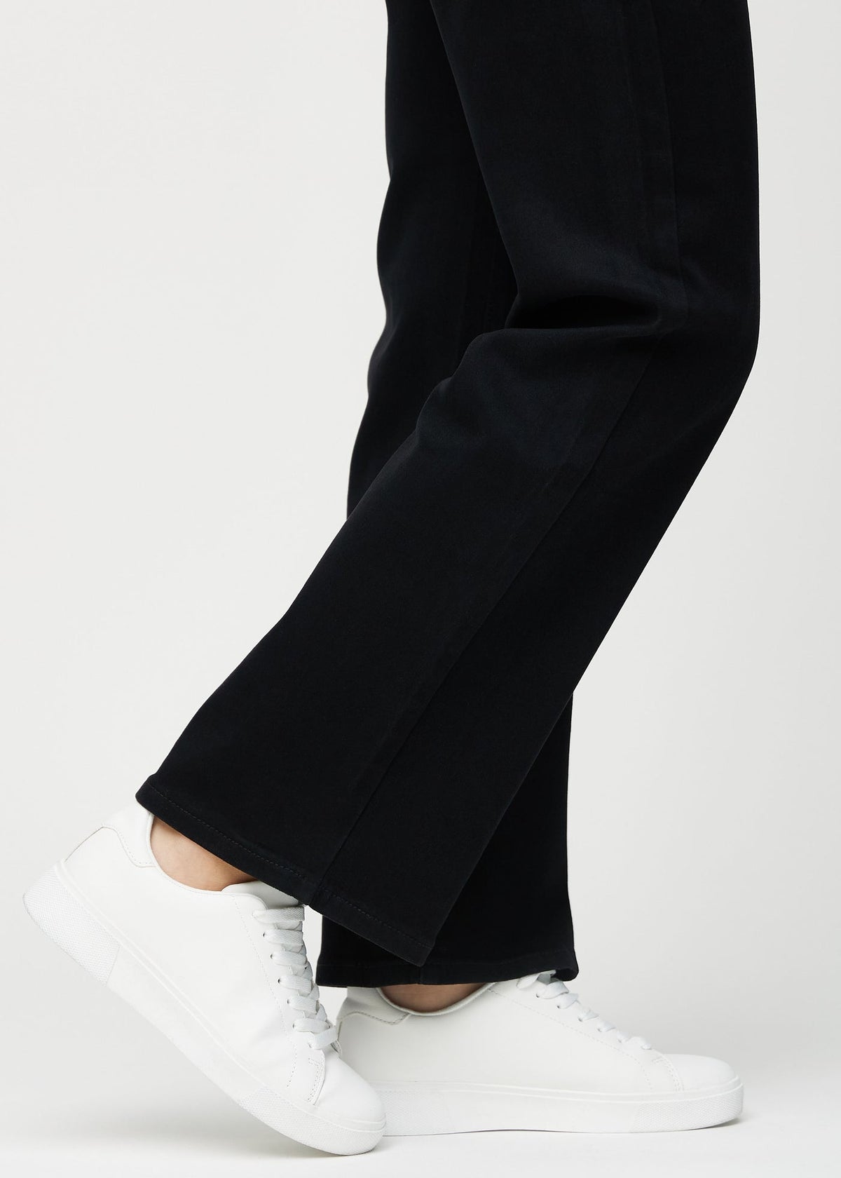 Close-up of the hem on BLAKC no-fade black jeans worn with white sneakers