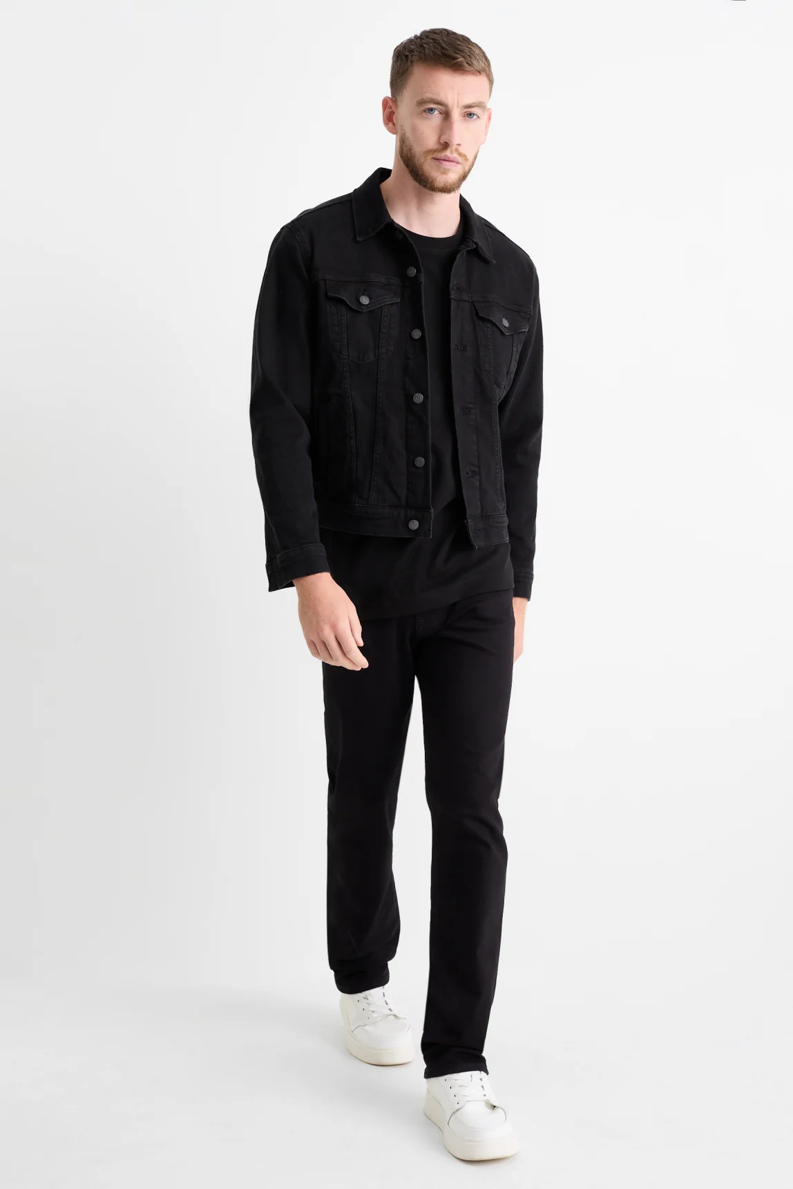 Man wearing a black denim jacket with BLAKC no-fade black jeans and white sneakers