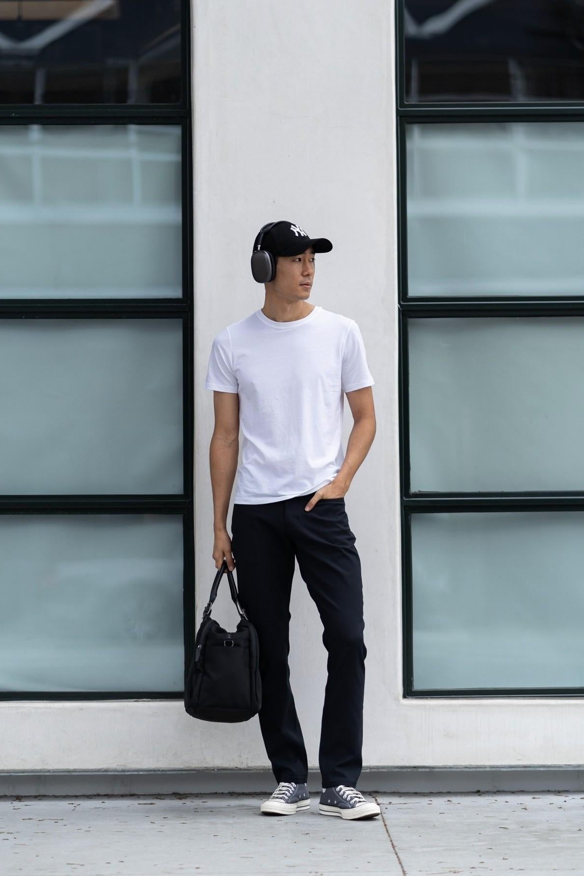 Man in a white t-shirt and BLAKC no-fade black jeans leaning against a wall