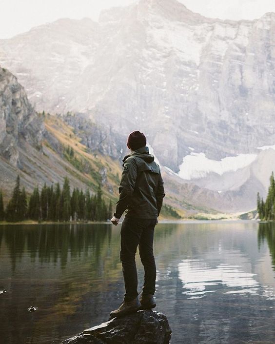 Person standing on a rock by a lake with mountains in the background