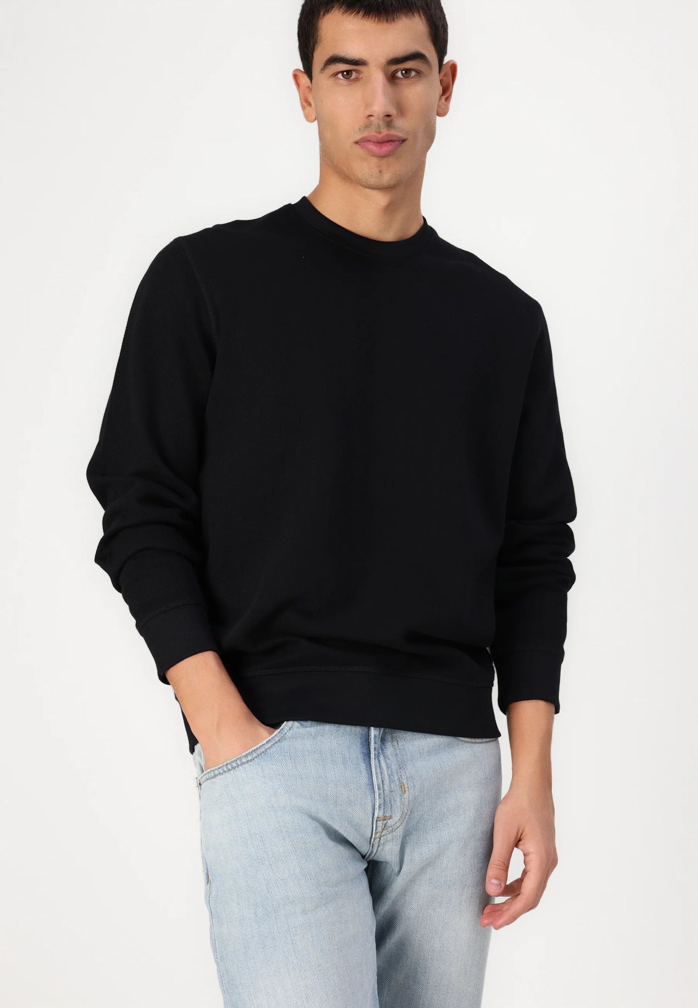 A man in a black crew-neck sweatshirt and light-wash jeans.