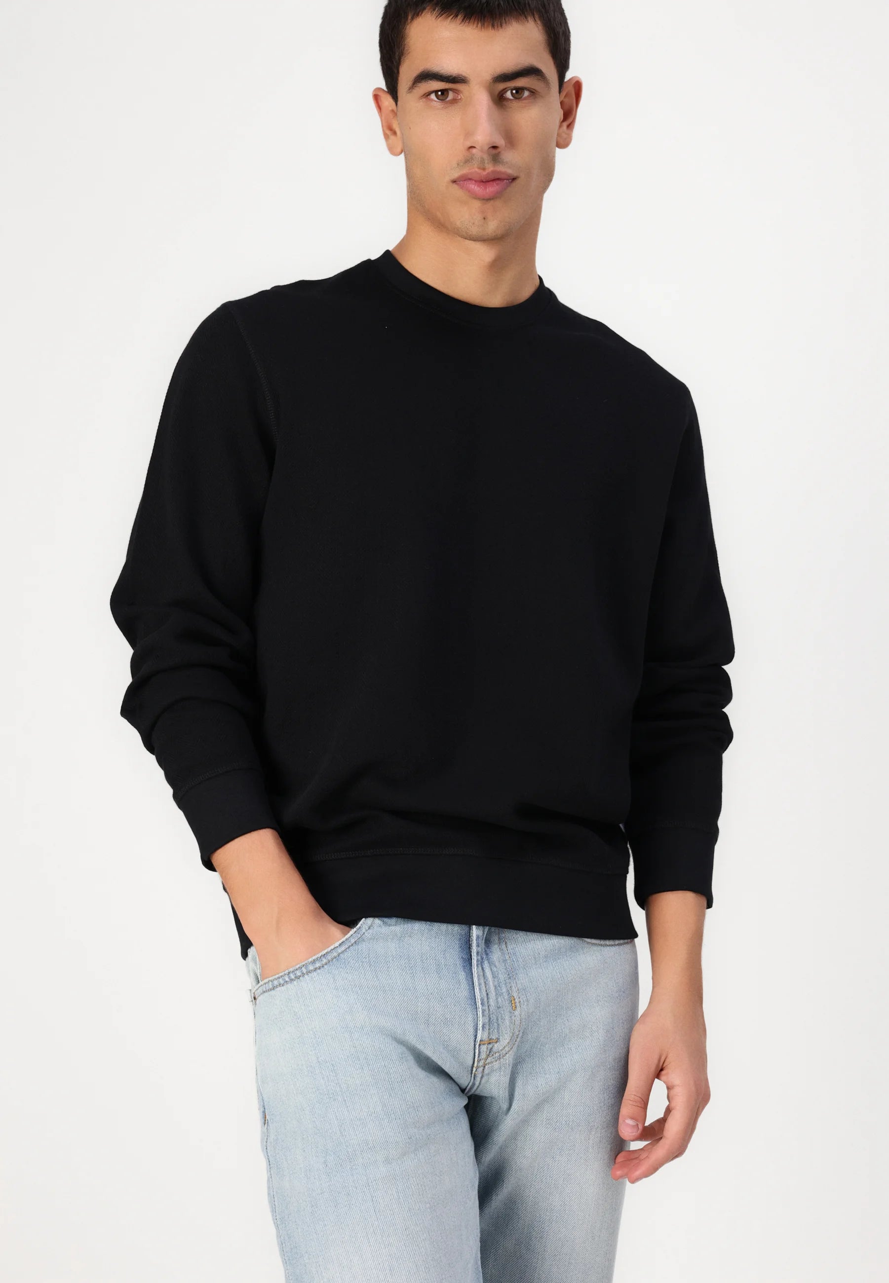 A man in a black crew-neck sweatshirt and light-wash jeans.